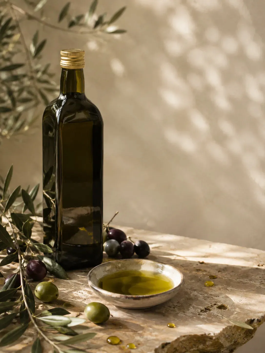 A bottle of olive oil beside a bowl of oil and olives